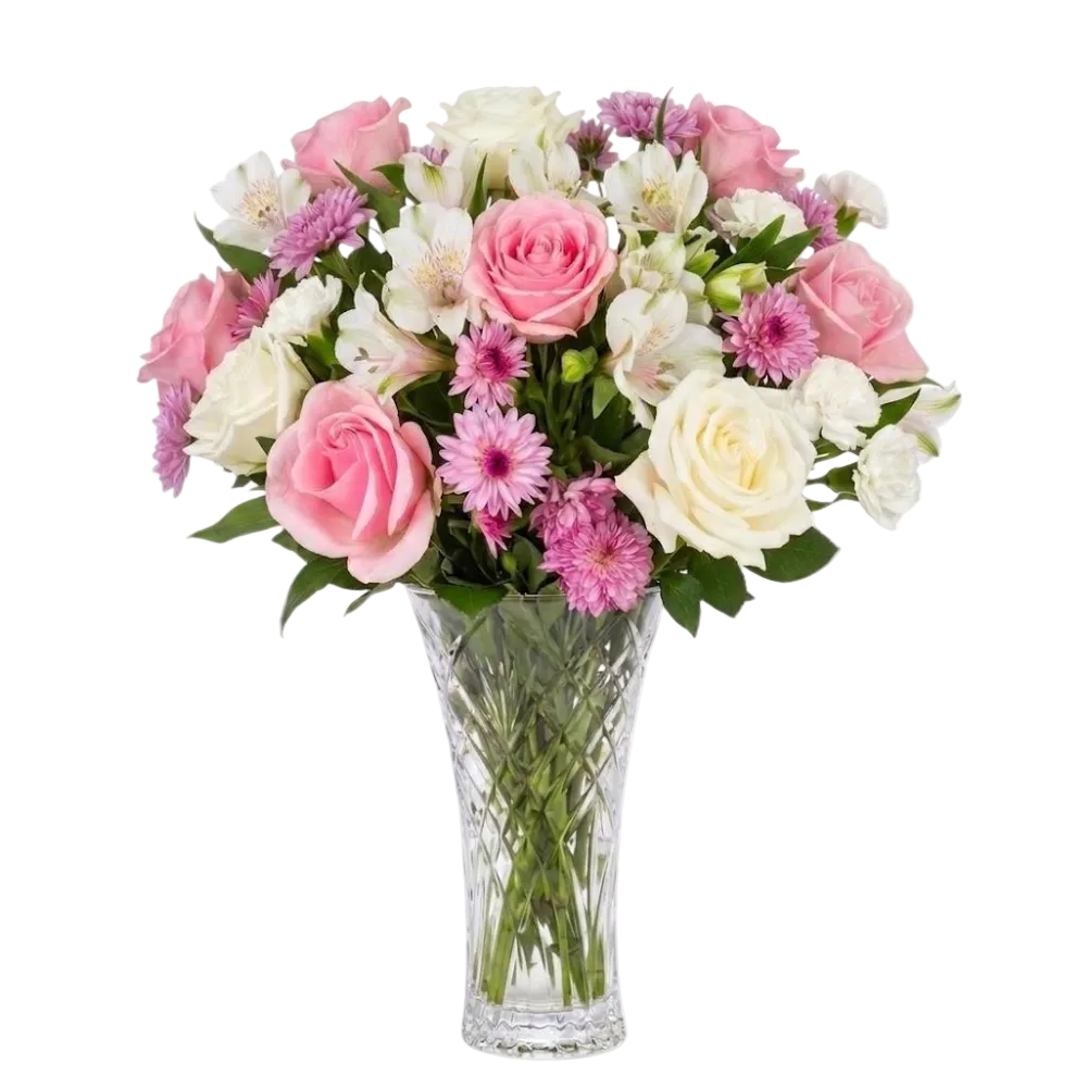 A vibrant floral bouquet featuring pink and white roses, white alstroemeria, pink daisies, and pink chrysanthemums arranged in a clear, faceted glass vase against a solid white background.