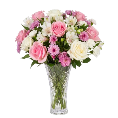 A vibrant floral bouquet featuring pink and white roses, white alstroemeria, pink daisies, and pink chrysanthemums arranged in a clear, faceted glass vase against a solid white background.